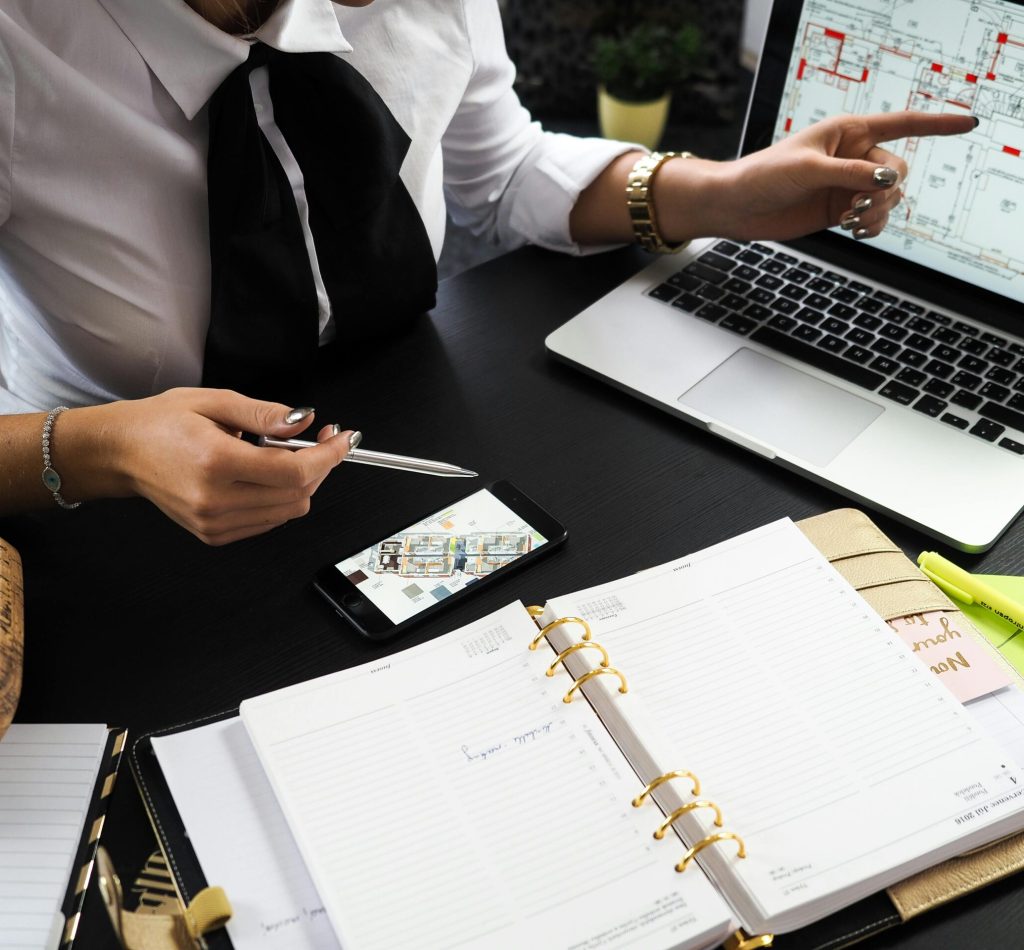 A business professional working on real estate project plans using multiple devices in an office setting.