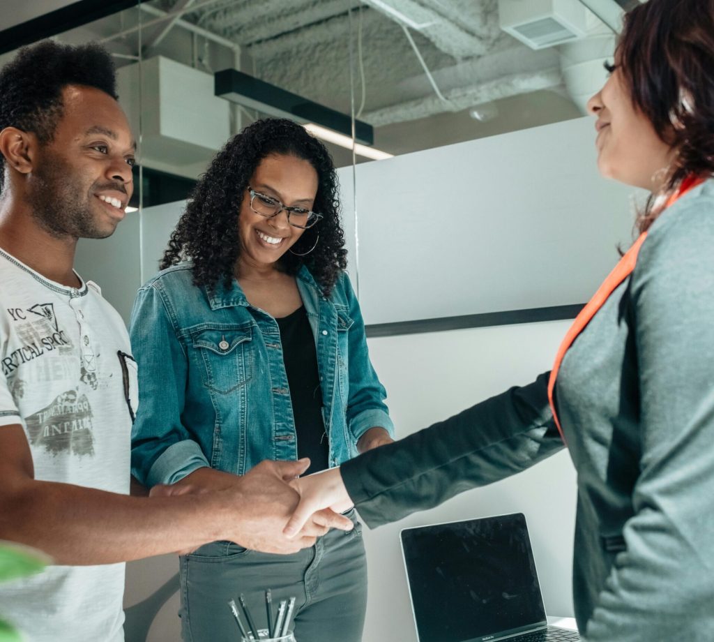 Smiling couple shaking hands with advisor in modern office.