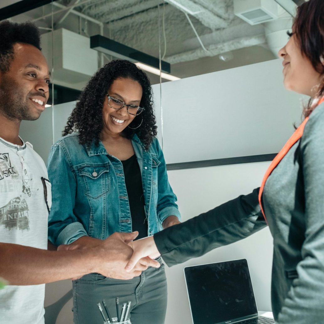 Smiling couple shaking hands with advisor in modern office.